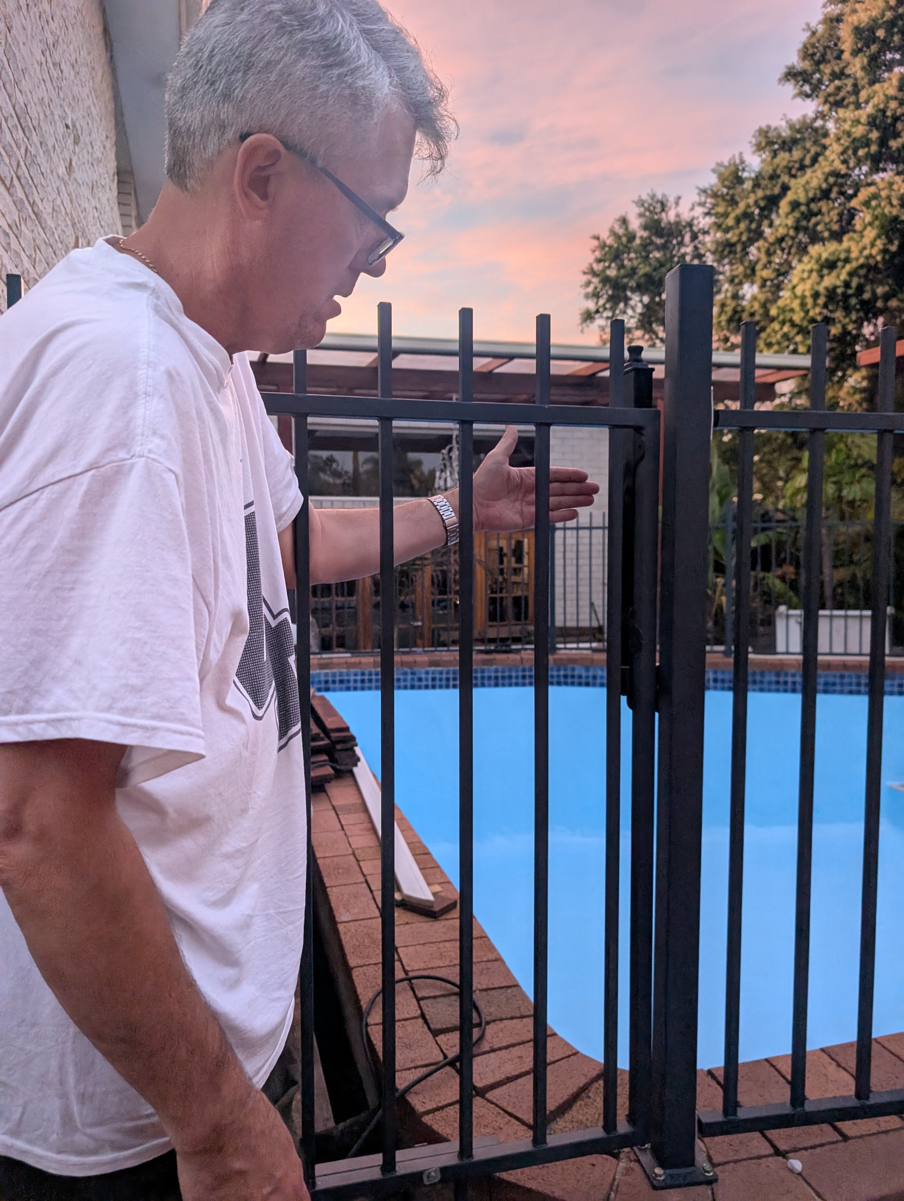 Black flat top pool fence and gate beside a swimming pool